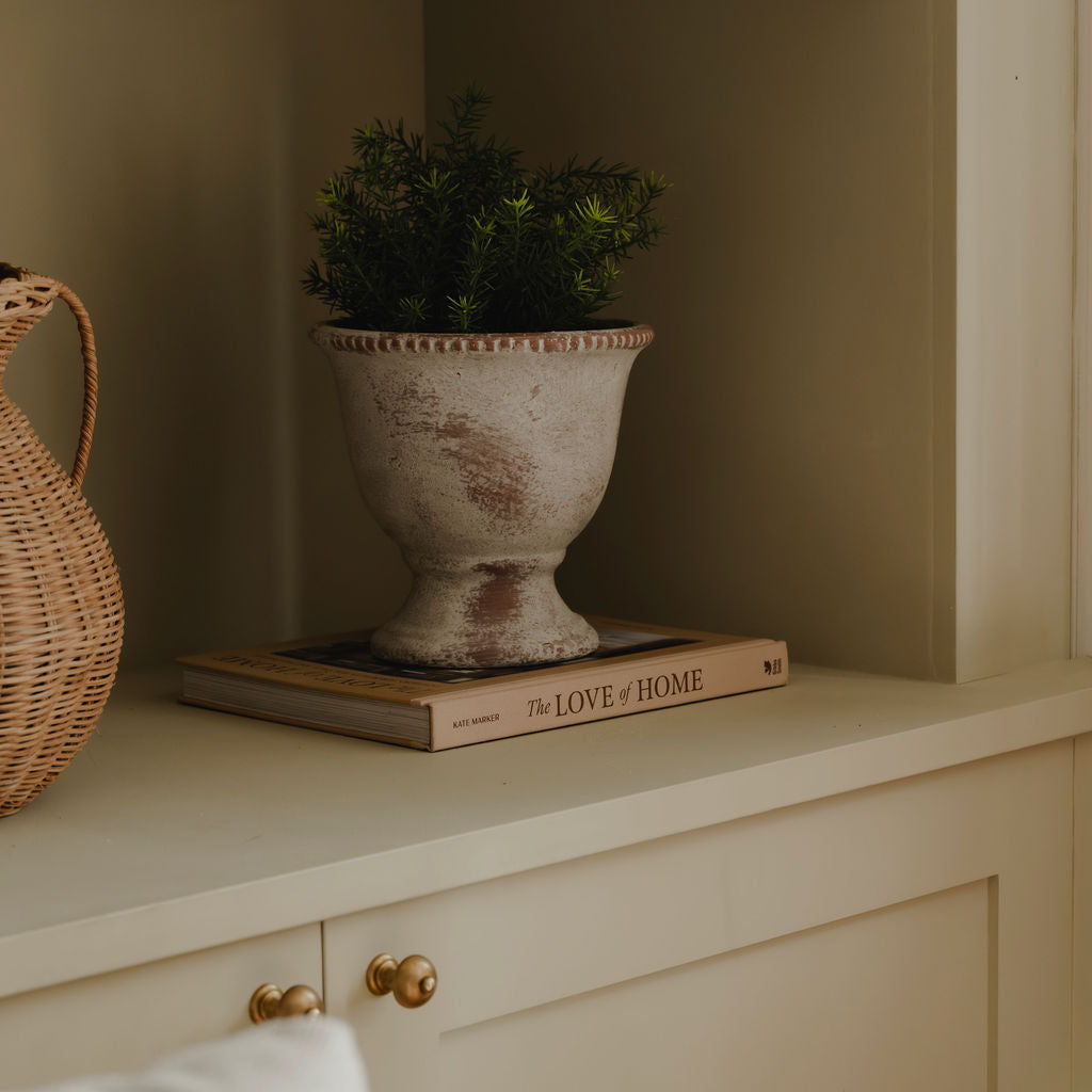 Decorative items including a plant in an urn, a woven basket, and a book titled 'The Love of Home' on a shelf.