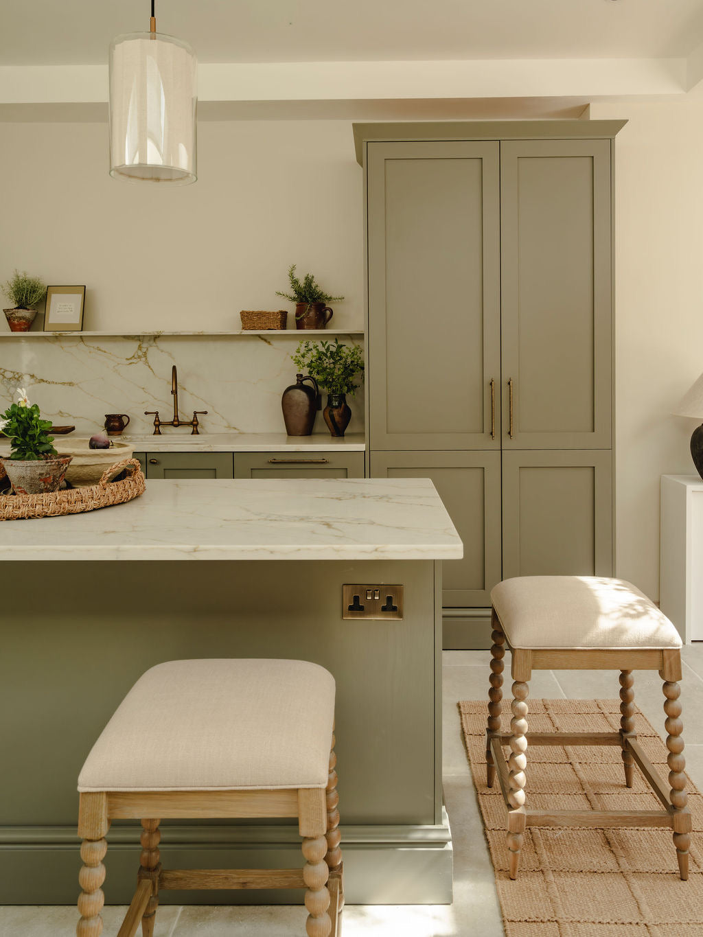 Modern kitchen with green cabinets, marble island, and wooden stools.