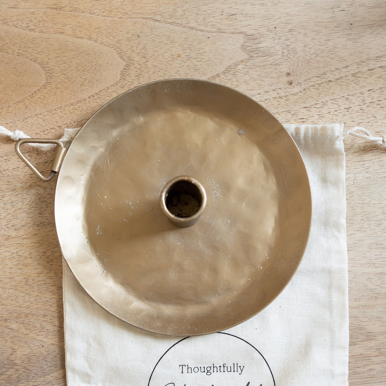 Brass lampshade on a branded cloth bag with 'Thoughtfully Handcrafted' logo on a wooden surface
