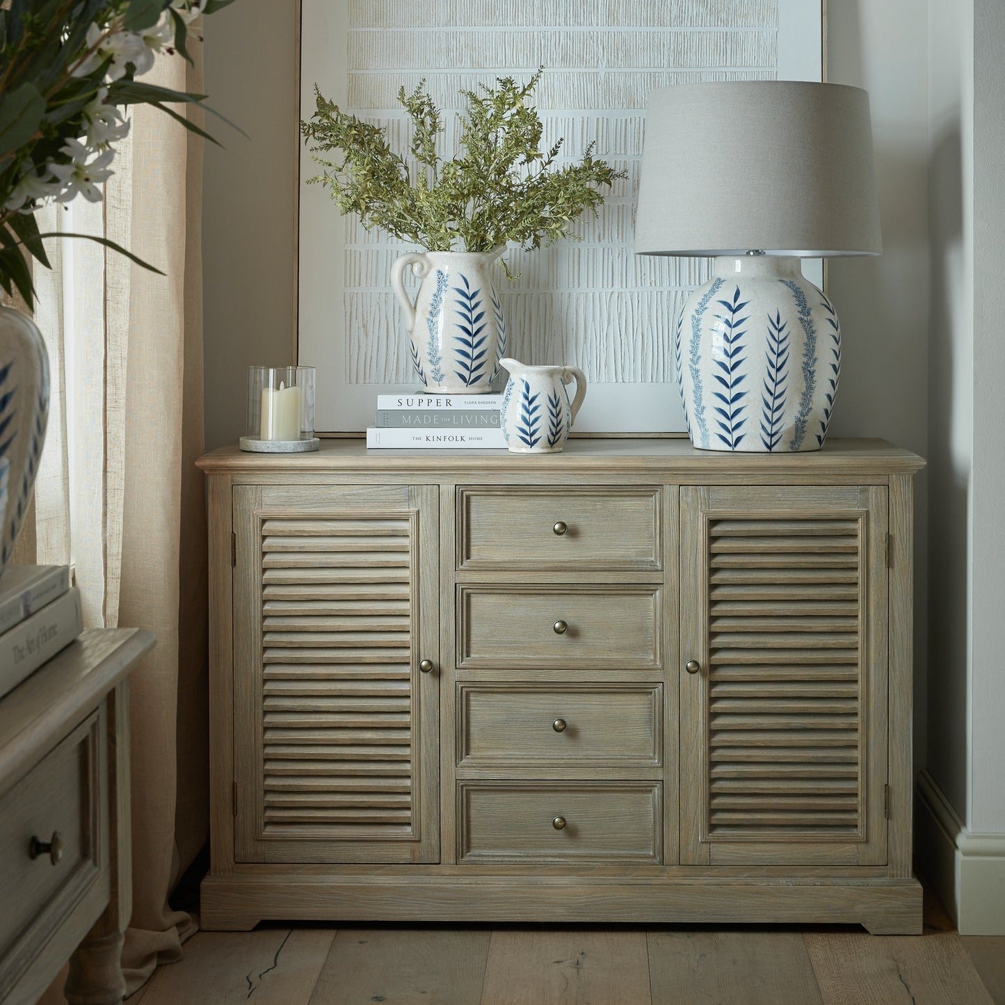 Wooden cabinet with decorative items including a lamp and vases in a room setting.