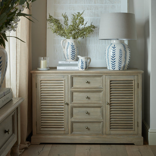 Wooden cabinet with decorative items including a lamp and vases in a room setting.