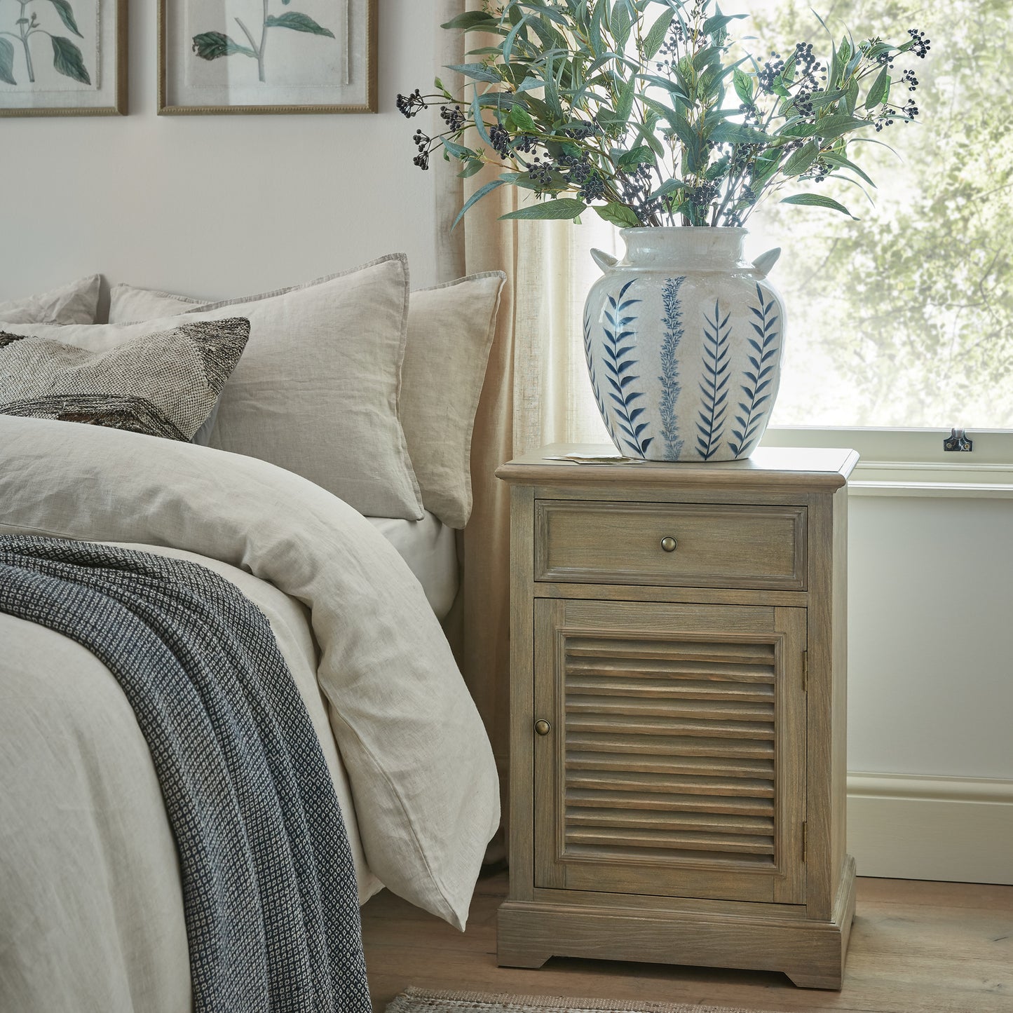 Bedroom with a wooden nightstand, bed with pillows, and vase with plants.