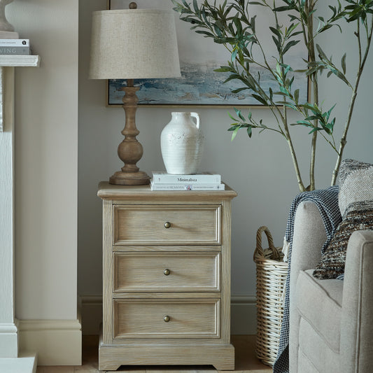 Light wood nightstand with lamp, books, and vase in a living room setting.