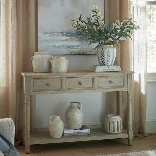 Light wooden console table with decorative items including vases and a painting in a room.
