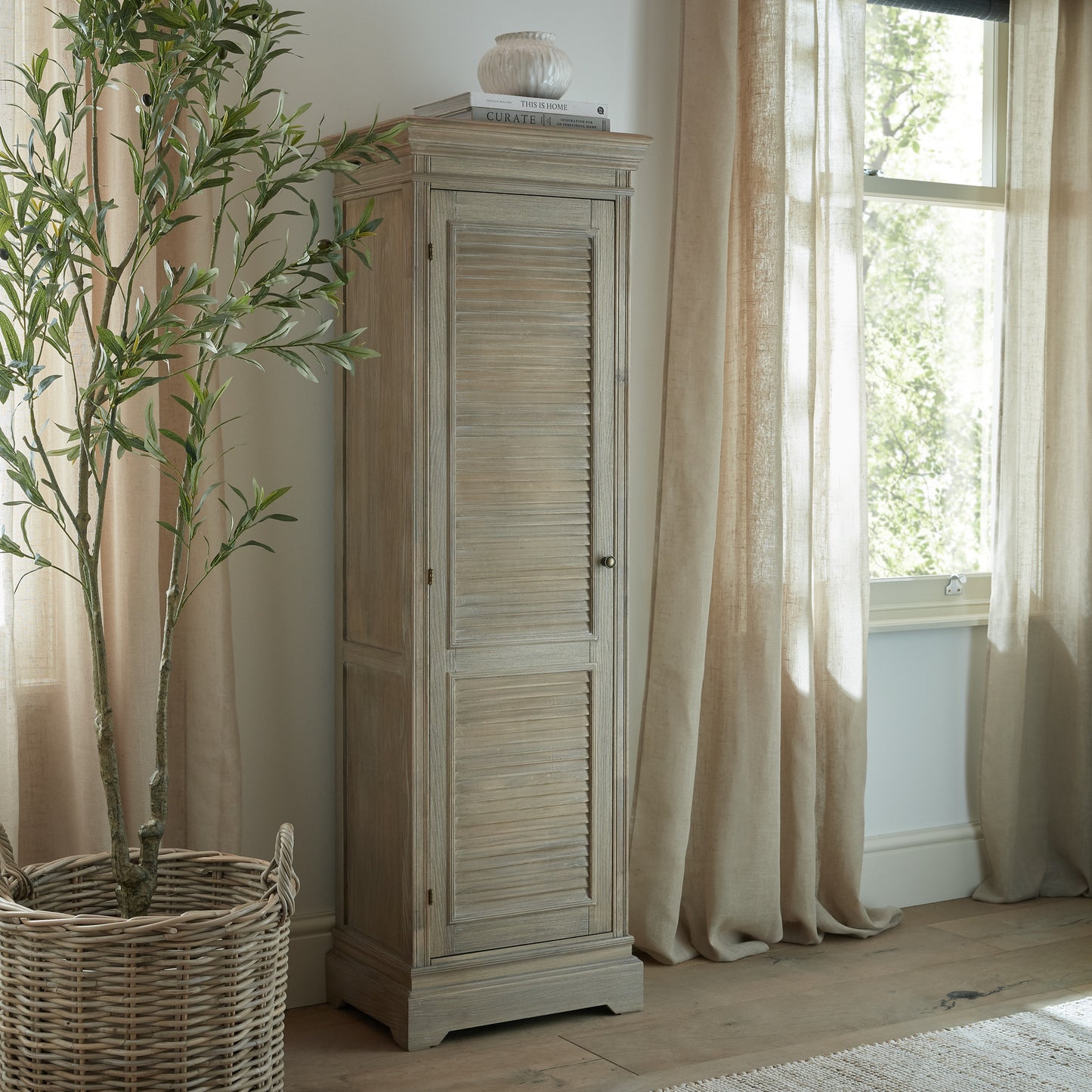 Wooden cabinet next to a window with curtains and a plant