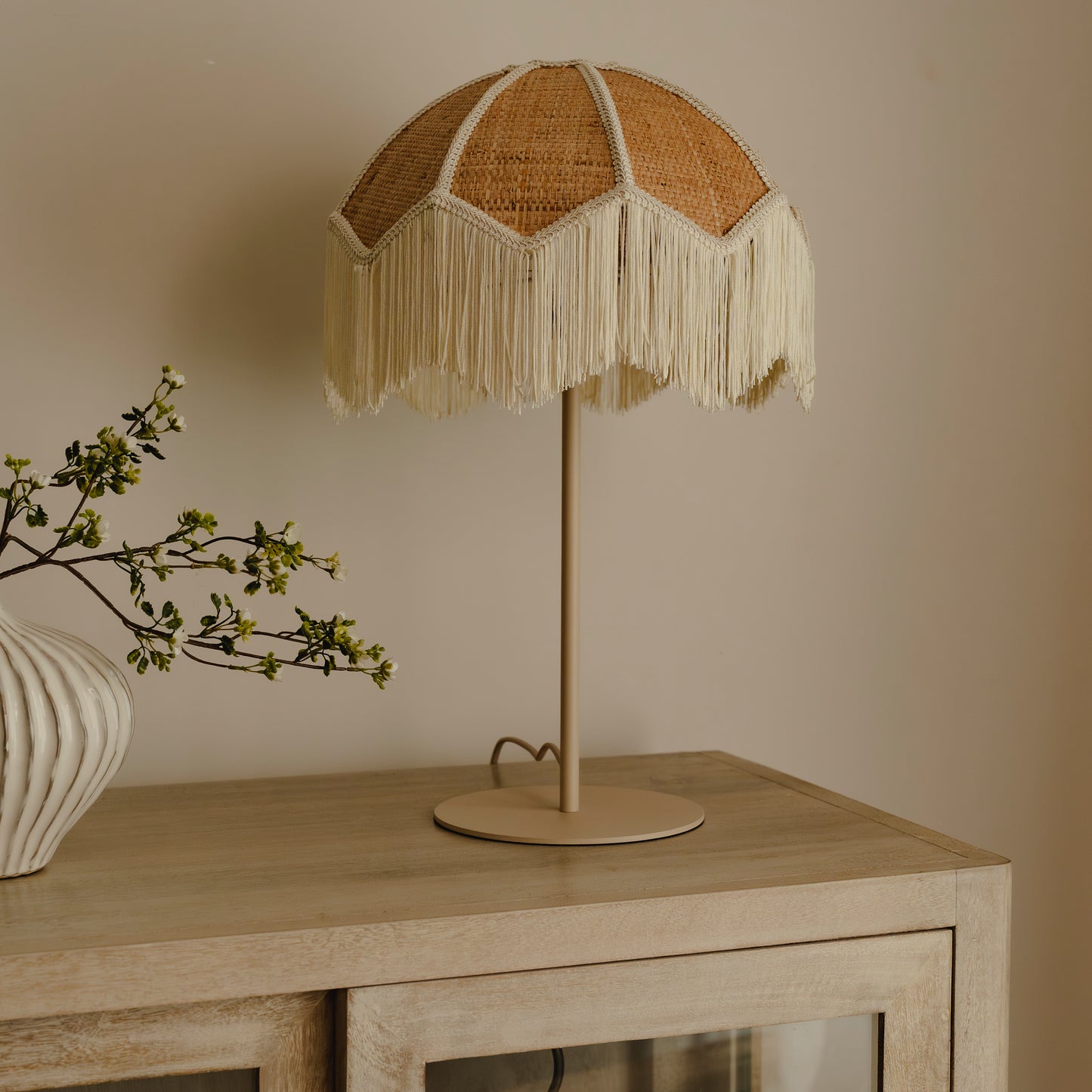 Table lamp with wicker shade on a wooden table against a beige wall
