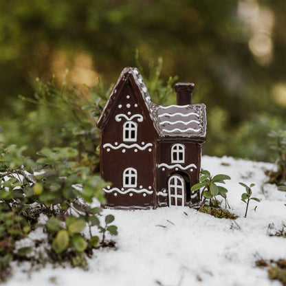 Miniature gingerbread house in a snowy landscape with greenery