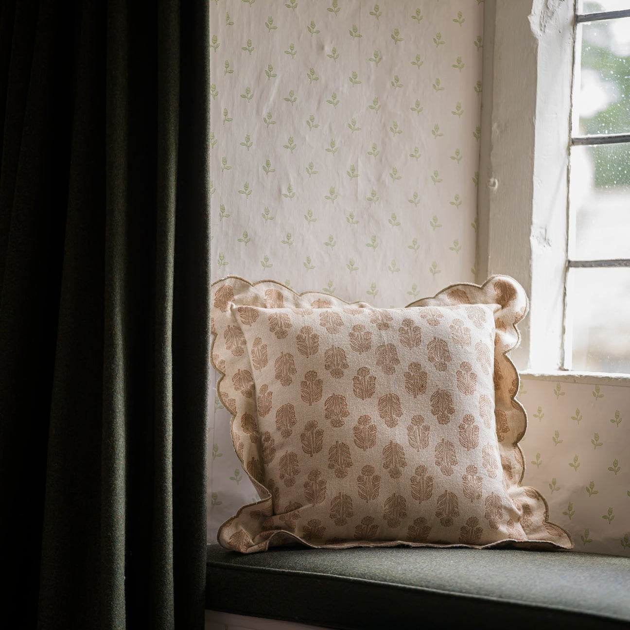 Decorative pillow on a window seat with patterned wallpaper and curtain.