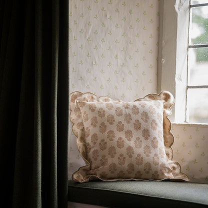 Decorative pillow on a window seat with patterned wallpaper and curtain.