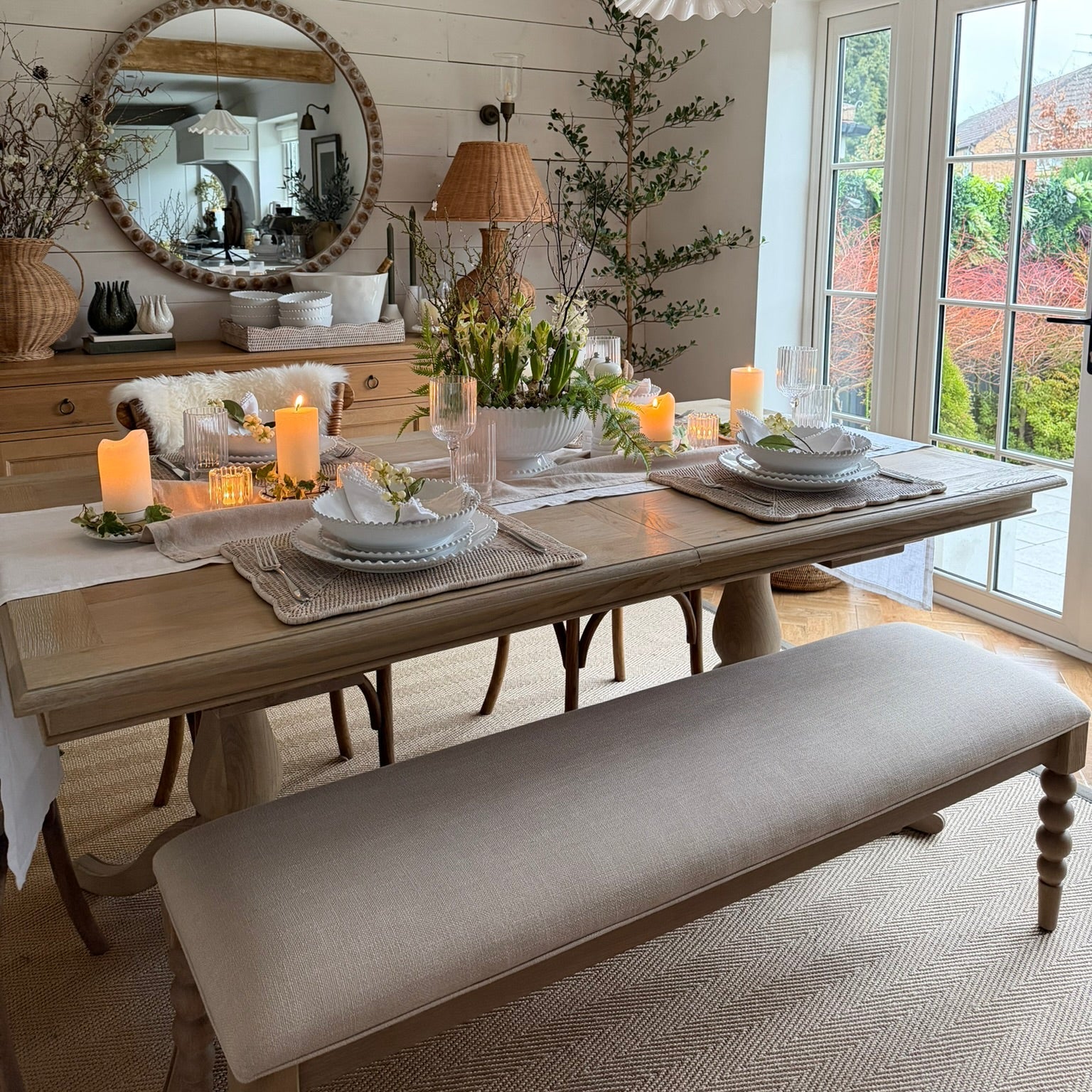 Dining room with a long wooden table set for a meal, featuring candles and place settings. A bench is in front of the table.