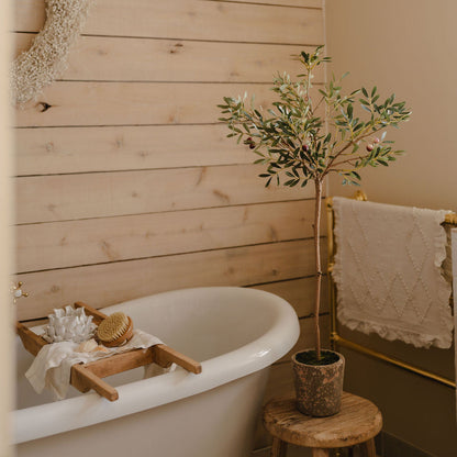 Bathroom with a white freestanding bathtub, wooden tray, and plant against a wooden wall.