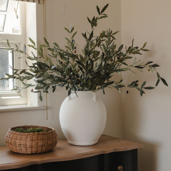 Real touch faux olive stems in a white vase beside a window