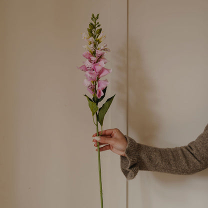 Person holding a pink artificial flower against a plain background