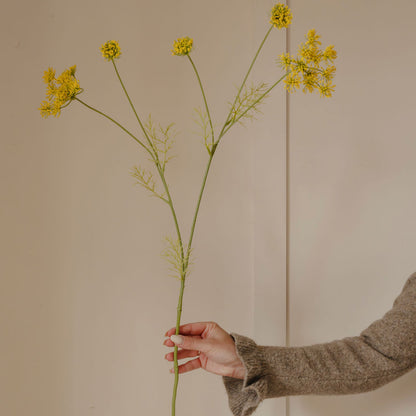 Hand holding a branch of yellow flowers against a beige background