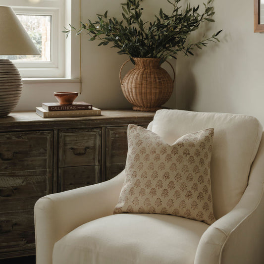 Cozy living room with a white armchair, decorative pillow, and a vase with greenery on a wooden side table.