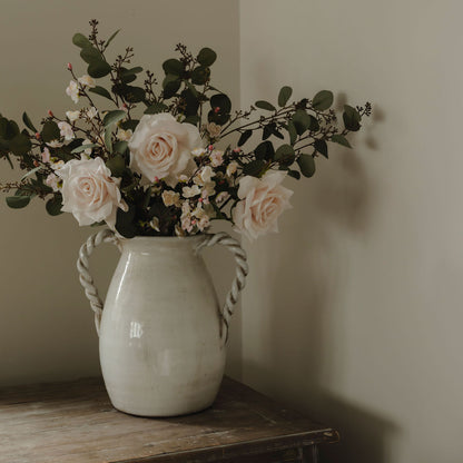 White vase with flowers on a wooden surface against a plain wall