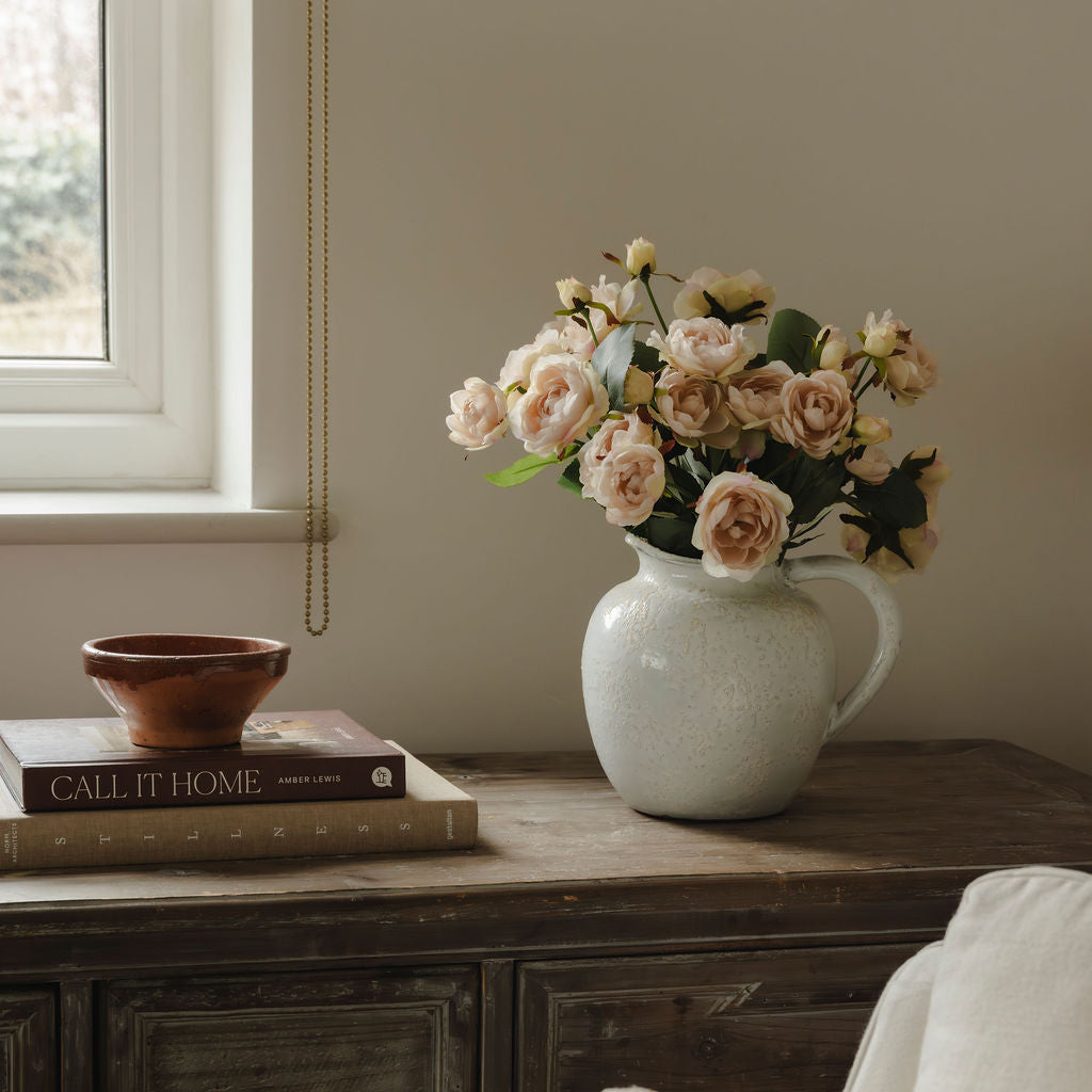Vase with flowers on a wooden side table next to books and a bowl.