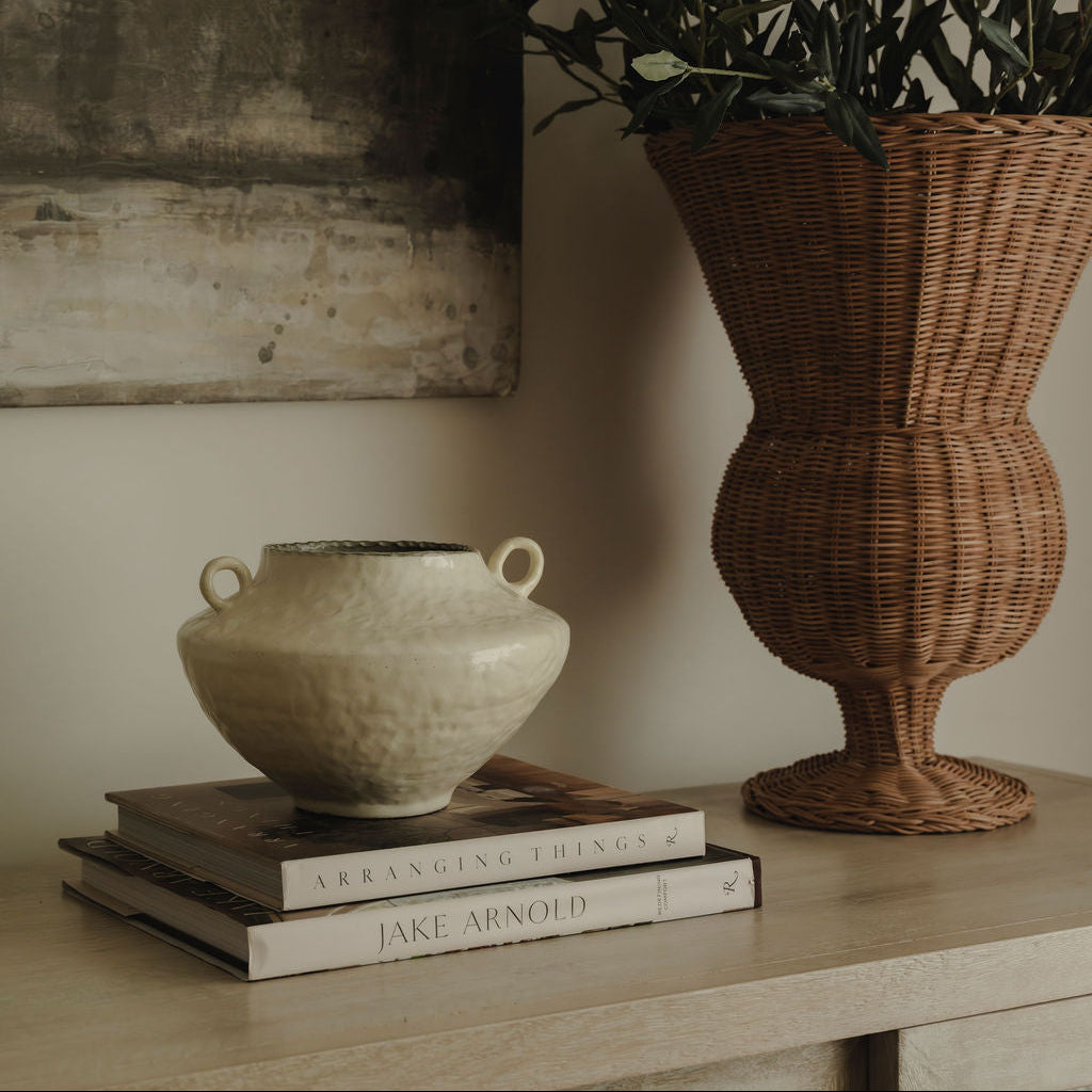 Decorative setup with a ceramic vase, wicker basket, and books on a wooden surface.