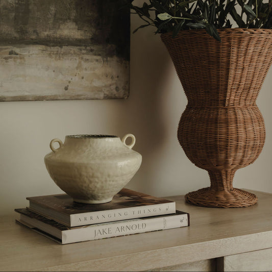 Decorative setup with a ceramic vase, wicker basket, and books on a wooden surface.