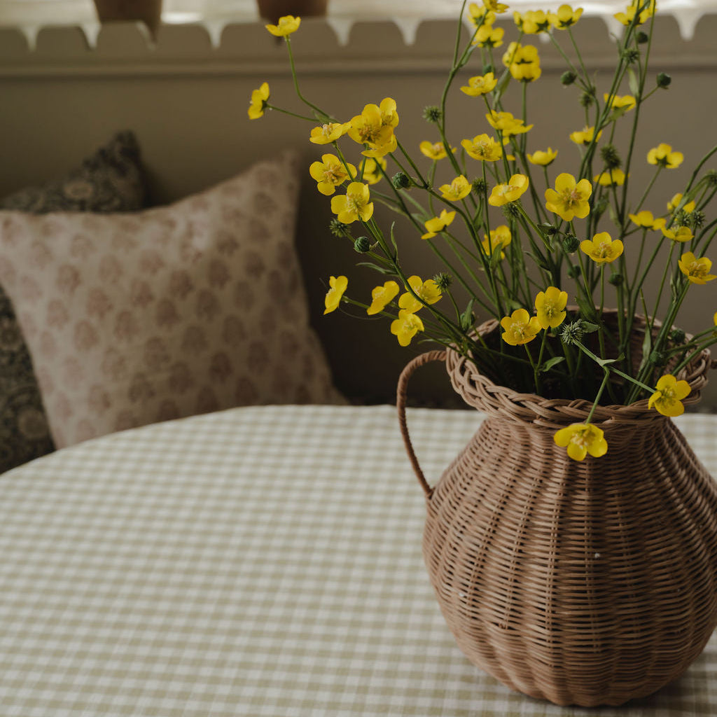 Wicker basket with yellow flowers on a checkered tablecloth, with plants in the background.