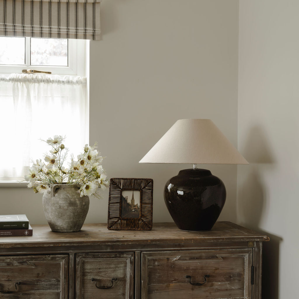 Decorative items on a wooden sideboard with a lamp, vase, and framed picture.