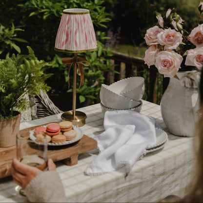 Outdoor setting with a table featuring a lamp, flowers, and macarons in a garden.