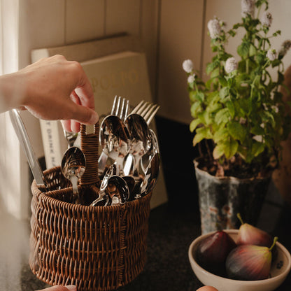 Person selecting cutlery from a basket with a plant and bowl of fruit in the background