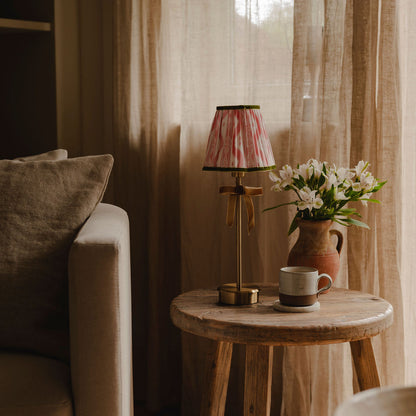 Small wooden table with a lamp, mug, and flowers against a curtain backdrop