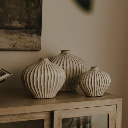 Three ribbed ceramic vases on a wooden surface with a neutral background