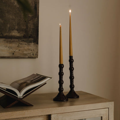 Two lit candles in black candlesticks on a wooden surface with an open book in the background.