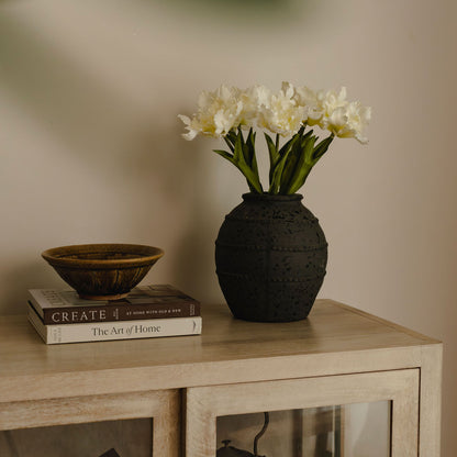Black textured vase with white flowers on a wooden surface