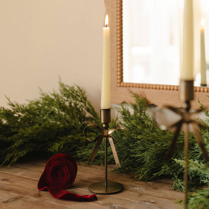 Decorative candle holder with a candle on a wooden surface with greenery and a red fabric roll.