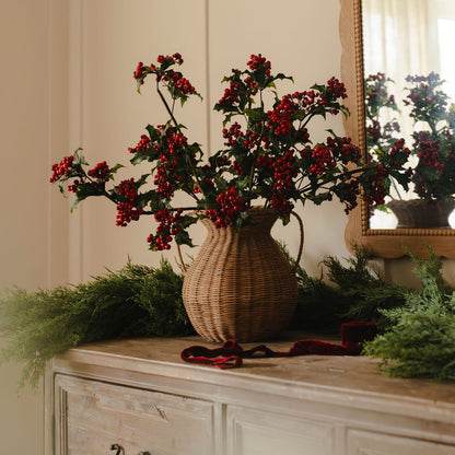 Decorative arrangement with red berries in a wicker vase on a wooden surface.