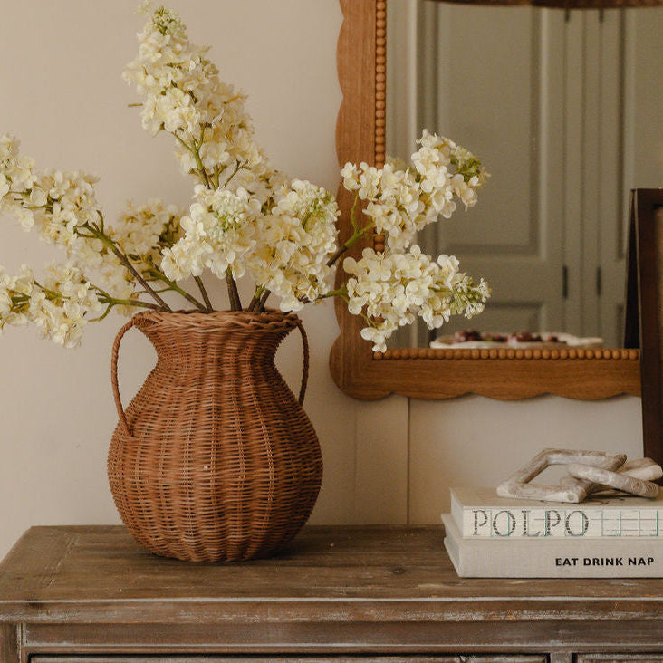 Woven wicker vase filled with white blossom on a wooden console beside a mirror