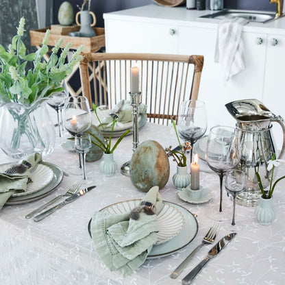 A set table featuring a small green ceramic bud vase as part of a table setting.
